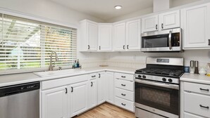 A modern kitchen with white cabinets, a stainless steel dishwasher, a gas stove, and a microwave. - Wonderfully Updated, Pet Friendly, Open Layout, Pool Table, BBQ, Next to Edgefield Golf and Concerts (Troutdale)