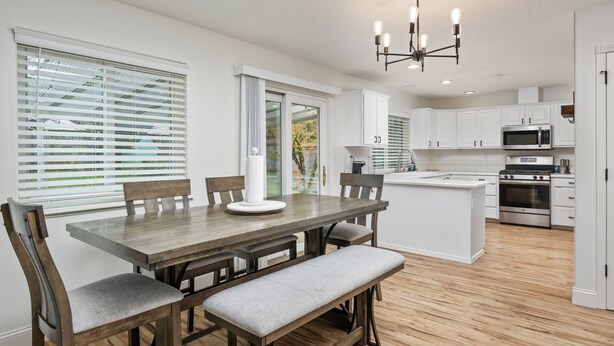 A modern kitchen with white cabinets, a central island, and a dining area with a wooden table and chairs. - Wonderfully Updated, Pet Friendly, Open Layout, Pool Table, BBQ, Next to Edgefield Golf and Concerts (Troutdale)