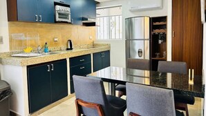 Una cucina moderna con mobili scuri, piani in granito, forno integrato e zona pranzo con tavolo e sedie in vetro.