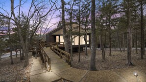 A cabin with a wooden deck and a staircase leading to the entrance. - Tree Top Hideaway – Pools, Sauna & More! (Lake Ozark)