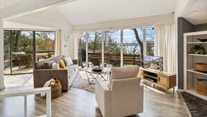 A spacious living room with a large window, a sofa, a coffee table, and a television. - Tree Top Hideaway – Pools, Sauna & More! (Lake Ozark)