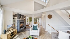 A spacious living area with a fireplace, a white armchair, a sofa, and a wooden coffee table. - Tree Top Hideaway – Pools, Sauna & More! (Lake Ozark)