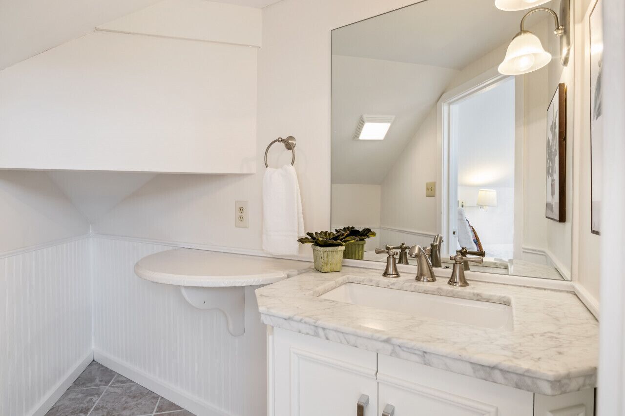 A bathroom with a white vanity, a sink, a mirror, and a towel rack.