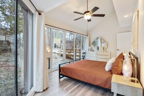 A bedroom with a bed, a ceiling fan, a dresser, a mirror, and large windows.