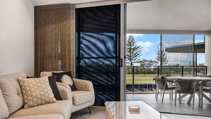Una sala moderna con sofá, mesa de centro y vista a un área de comedor exterior a través de una puerta corrediza de vidrio.