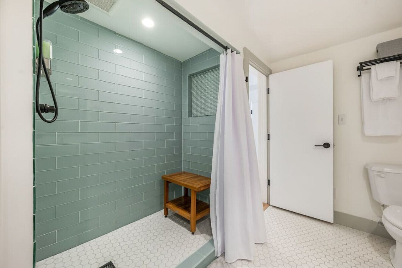 A bathroom with a shower, a toilet, and a small wooden stool.