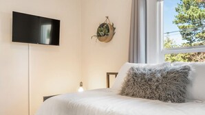 Ein Schlafzimmer mit Bett, montiertem Fernseher, hängender Pflanze und einem Fenster mit Blick auf Bäume.