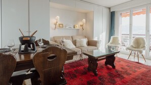 Ein modernes Wohnzimmer mit Essbereich, einer Sofagarnitur, einem roten Teppich mit Muster und einem Balkon mit Blick.