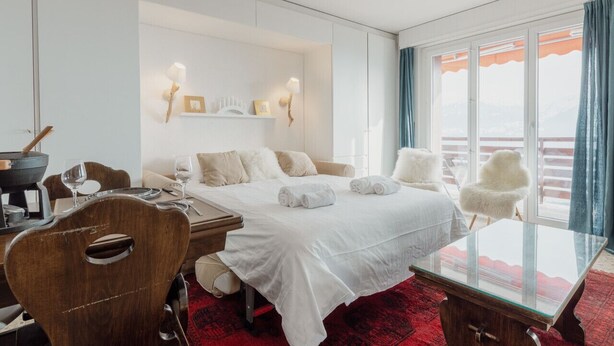 Ein Hotelzimmer mit einem Bett, einem Glastisch, einem Holzsessel, einem roten Teppich und einem Balkon mit Blick.