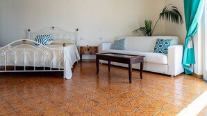 Una habitación con cama, sofá, una pequeña mesa y una planta en maceta.