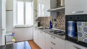 Una cocina compacta con armarios blancos, estufa a gas y salpicadero de azulejos.