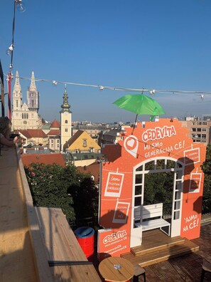 Una terraza en la azotea con vistas a un paisaje urbano, un paraguas verde y un letrero que dice 'CEDEVITA'.