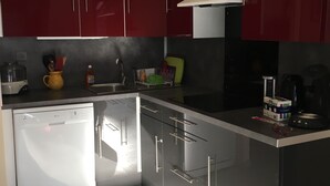 A modern kitchen with red cabinets, a dishwasher, and a coffee machine. - Rent House in Residence (Argelès-sur-Mer)
