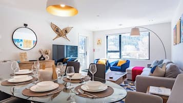 Una sala de estar moderna con una mesa redonda de vidrio dispuesta para comer, un sofá y un ventanal con vistas.