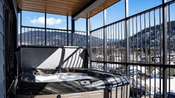 Un jacuzzi en un balcón con vistas a montañas y un estacionamiento.