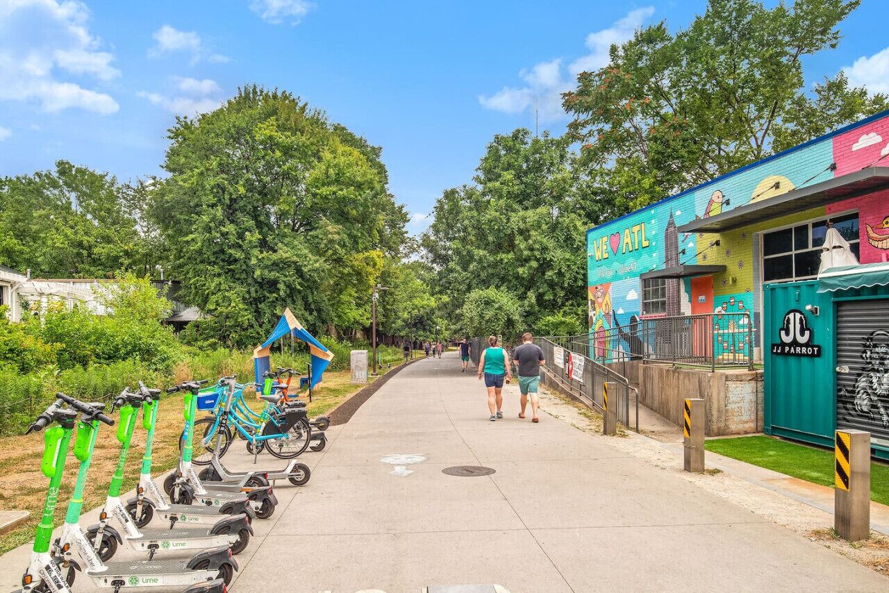 A pathway lined with electric scooters and bicycles, a mural on a building, and a storefront with a sign.
