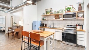 A modern kitchen with a wooden table and chairs, a built-in oven, a microwave, and a sink. There are shelves above the counter with decorative items and plants. - Walker's Paradise + Espresso Machine + King Bed (Atlanta)