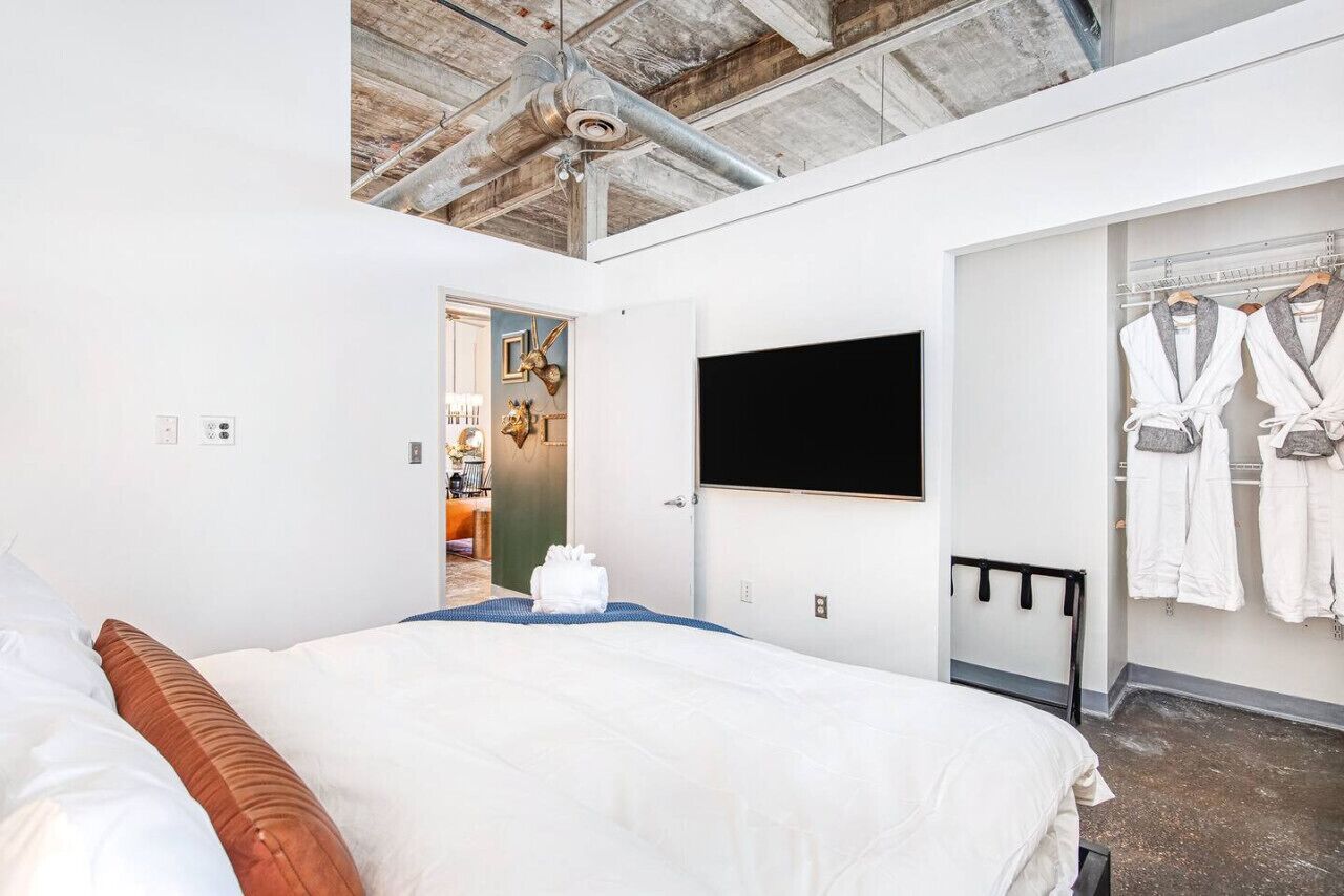 Una habitación de hotel con una cama, un televisor de pantalla plana montado en la pared y un vestidor con batas.