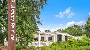 A building with a white exterior and a porch, surrounded by greenery. - Walker's Paradise + Espresso Machine + King Bed (Atlanta)