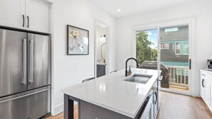 A modern kitchen with stainless steel appliances, a large island, and a sliding glass door leading to a balcony. - Second Floor Balcony | EV Charger |King Bed (Atlanta)