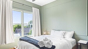 A bedroom with a large bed, white bedding, a blue throw blanket, and a view of the outside. - Second Floor Balcony | EV Charger |King Bed (Atlanta)