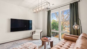 A modern living room with a large flat-screen TV, a leather sofa, a white armchair, and a dining table. - Fast Wifi|Downtown EAV| EAV Retreat (Atlanta)