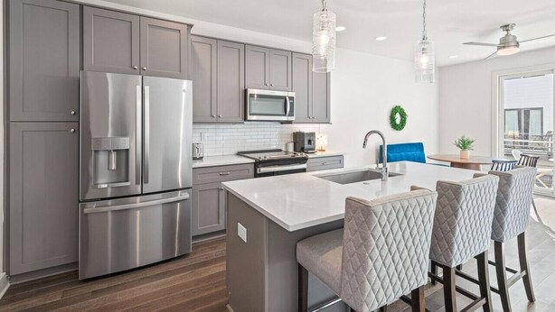 A modern kitchen with grey cabinets, stainless steel appliances, a central island with bar stools, and pendant lighting. - Fast Wifi|Downtown EAV| EAV Retreat (Atlanta)