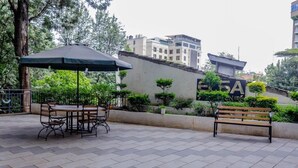 Een terras buiten met een tafel, stoelen, een bank en een grote parasol.