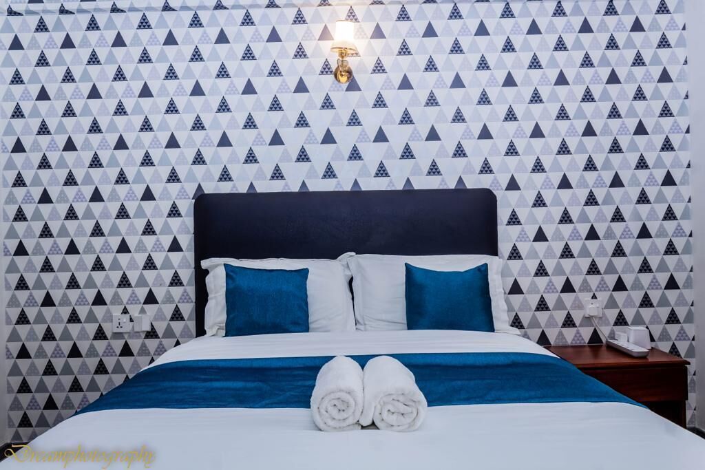 A hotel room with a patterned wallpaper, a bed with blue and white bedding, and a pair of rolled towels on the bed.