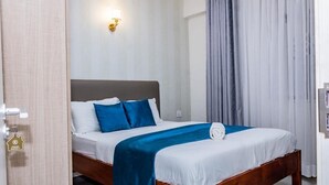 Een net opgemaakt bed met een blauw-witte spreideken, een houten hoofdbord en een wandlamp.