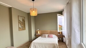 A bedroom with a bed, a hanging light fixture, a bedside table, and a window with curtains. - House near the city center, beaches and train station. Sea view, terrace. (Bandol)