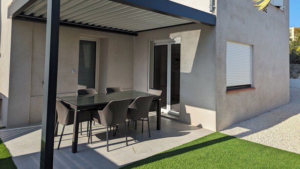 A covered outdoor dining area with a table and chairs, a pergola, and a view of a building with windows and a door. - House near the city center, beaches and train station. Sea view, terrace. (Bandol)