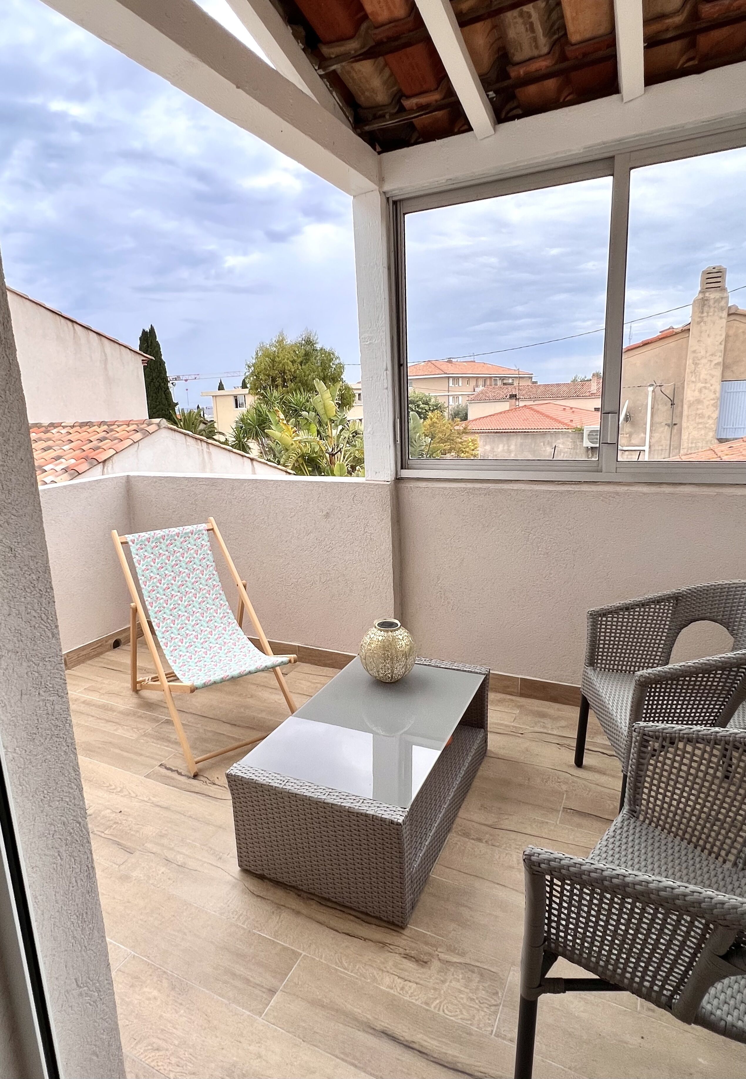 A covered outdoor area with a wicker sofa, a small table with a vase, and a folding chair.