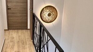 A hallway with a wooden door, a black metal railing, and a wall-mounted light fixture. - House near the city center, beaches and train station. Sea view, terrace. (Bandol)