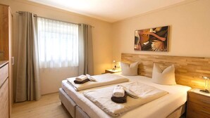 A hotel room with two beds, a wooden headboard, a painting, and a nightstand with a lamp. - Tranquil apartment in the centre of Seefeld (Seefeld in Tirol)