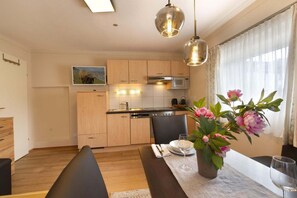 A modern kitchen with wooden cabinets, a dining table with a vase of flowers, and a bench.
