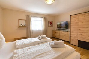 A hotel room with two beds, a TV, a wooden wardrobe, and a window with curtains.