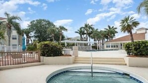 A swimming pool with a fountain, surrounded by palm trees and a covered area with steps leading up to a building.