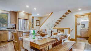 Una cocina moderna con armarios de madera, un refrigerador de acero inoxidable y una zona de comedor con mesa y bancos de madera.