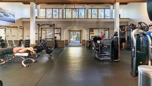 Academia com diversos equipamentos de exercício, um arco central e amplas janelas que permitem entrada de luz natural.