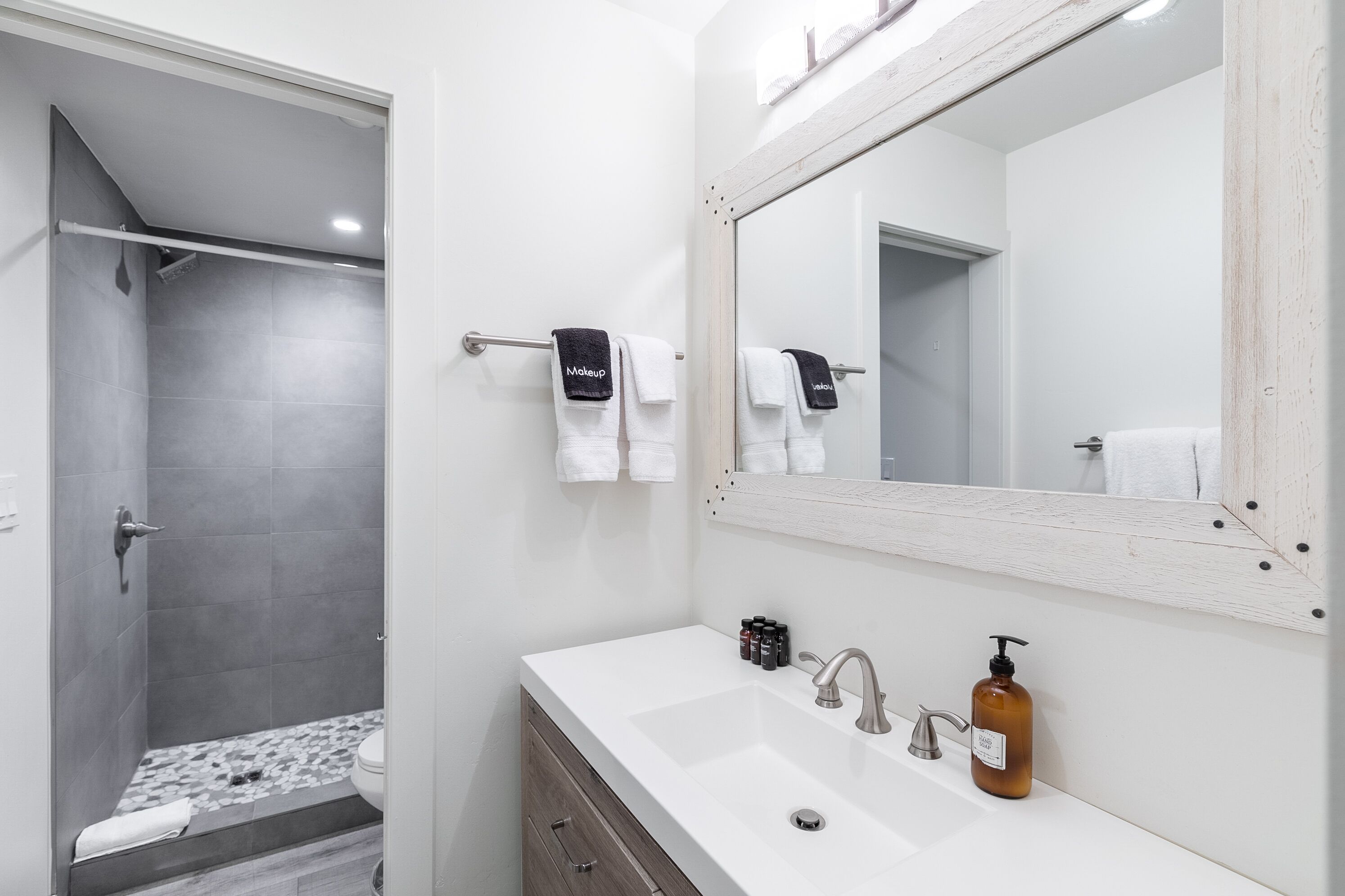 A modern bathroom with a shower, a large mirror, and a white sink with a soap dispenser.