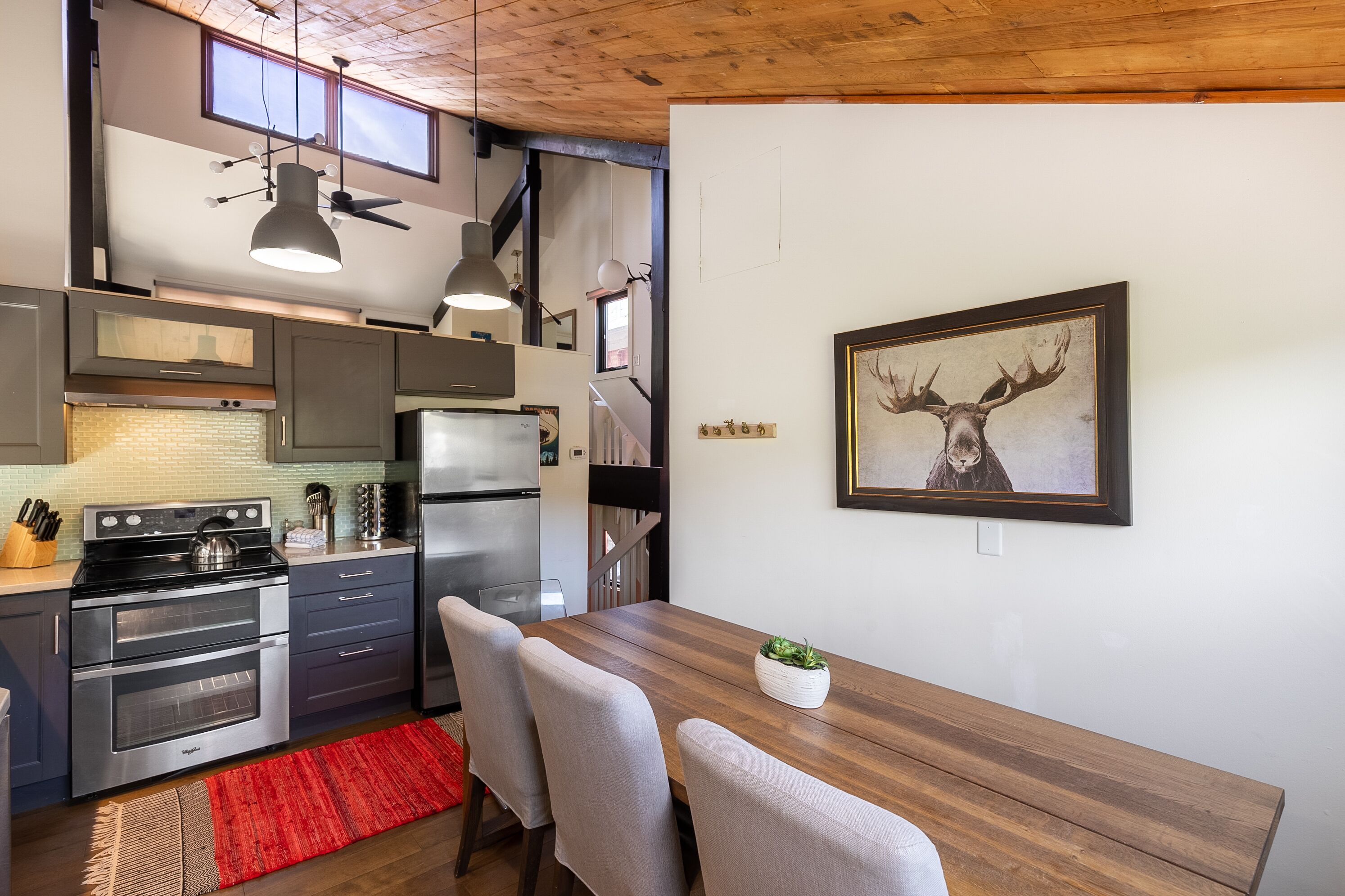 Een moderne keuken met roestvrijstalen apparatuur, een houten eettafel en een afbeelding van een hertenhoofd in een lijst aan de muur.