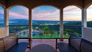 Un balcon offrant une vue sur une vallée et des montagnes, avec trois chaises et une table.