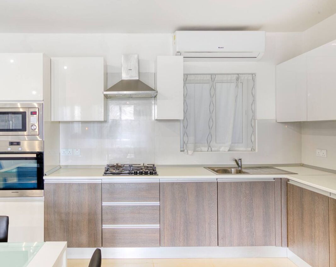 Une cuisine moderne avec des meubles blancs, un four à micro-ondes encastré, une cuisinière et une fenêtre avec des rideaux.