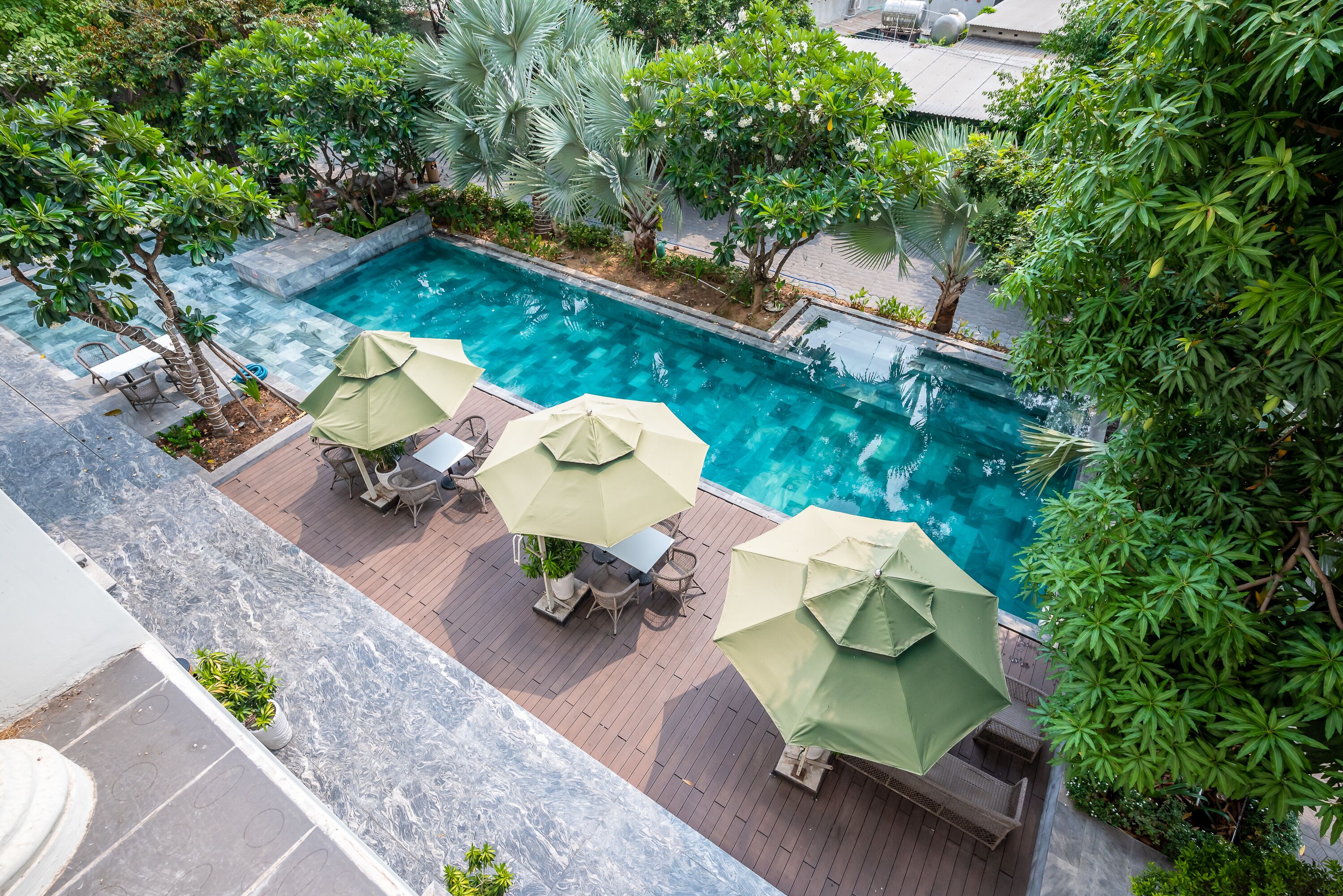 A rooftop pool area with a clear view of the pool, surrounded by lush greenery and outdoor seating with umbrellas.