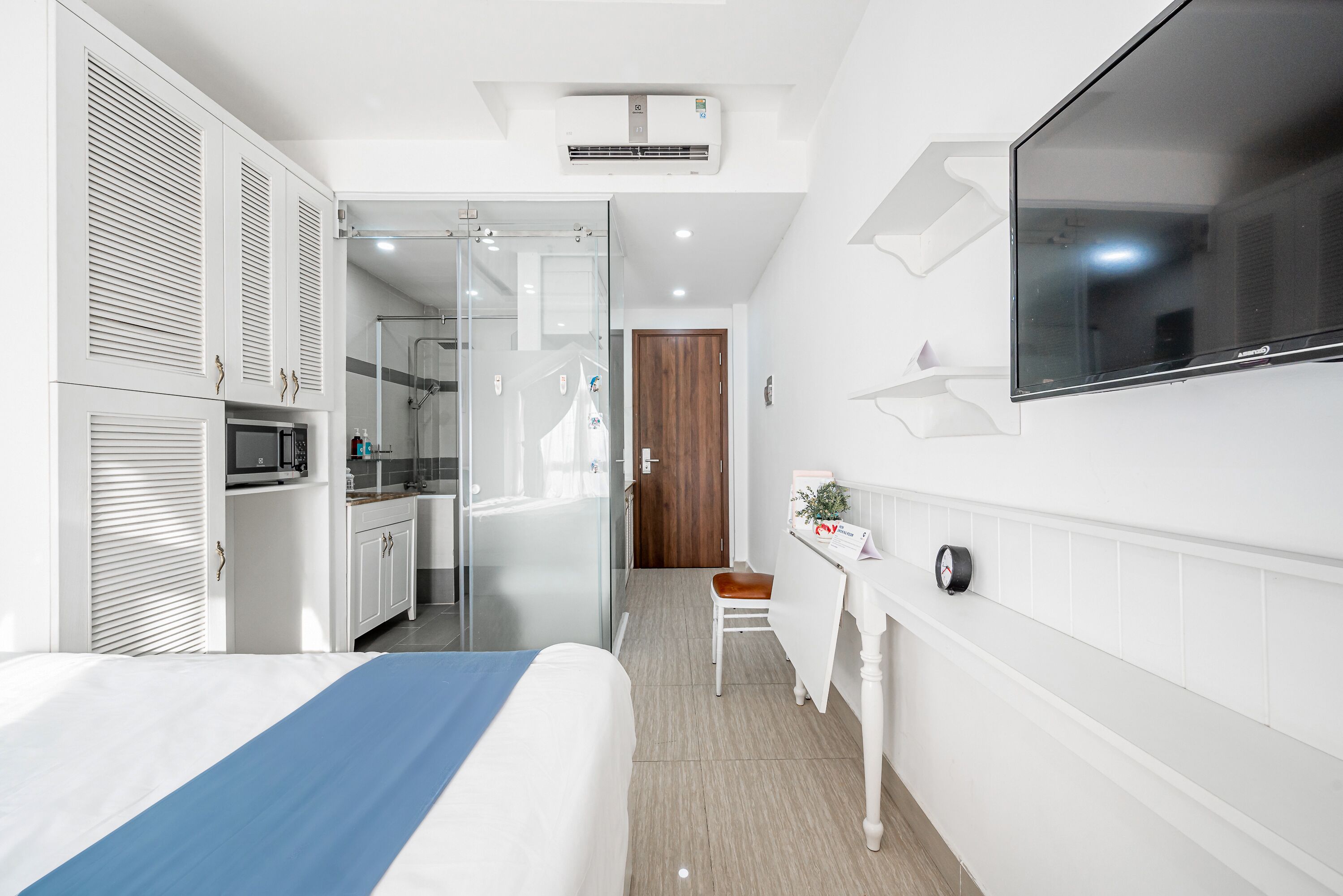 A modern hotel room with a bed, a desk, a microwave, and a shower area.