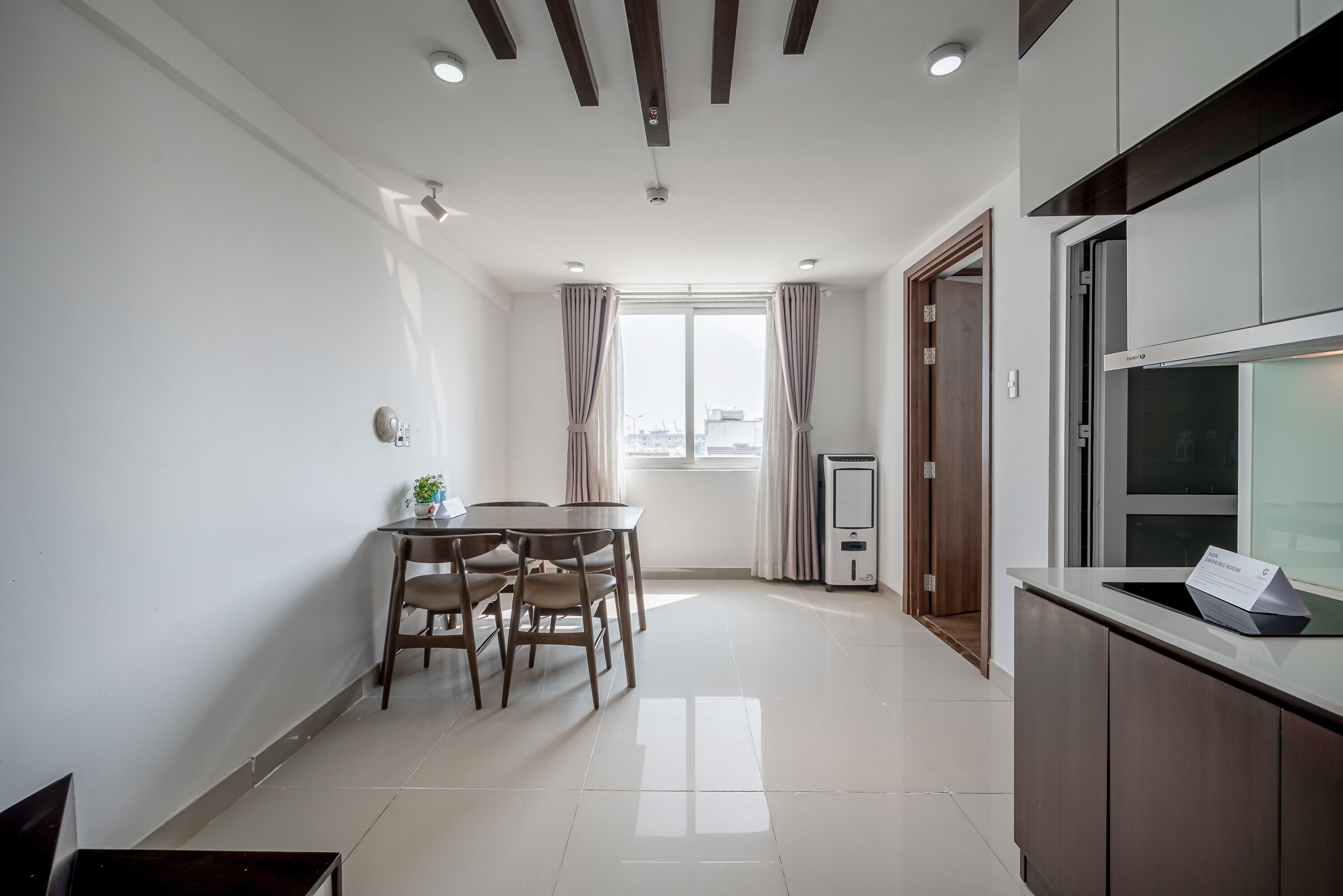 A modern kitchen with a dining area, a large window with curtains, and a built-in oven.