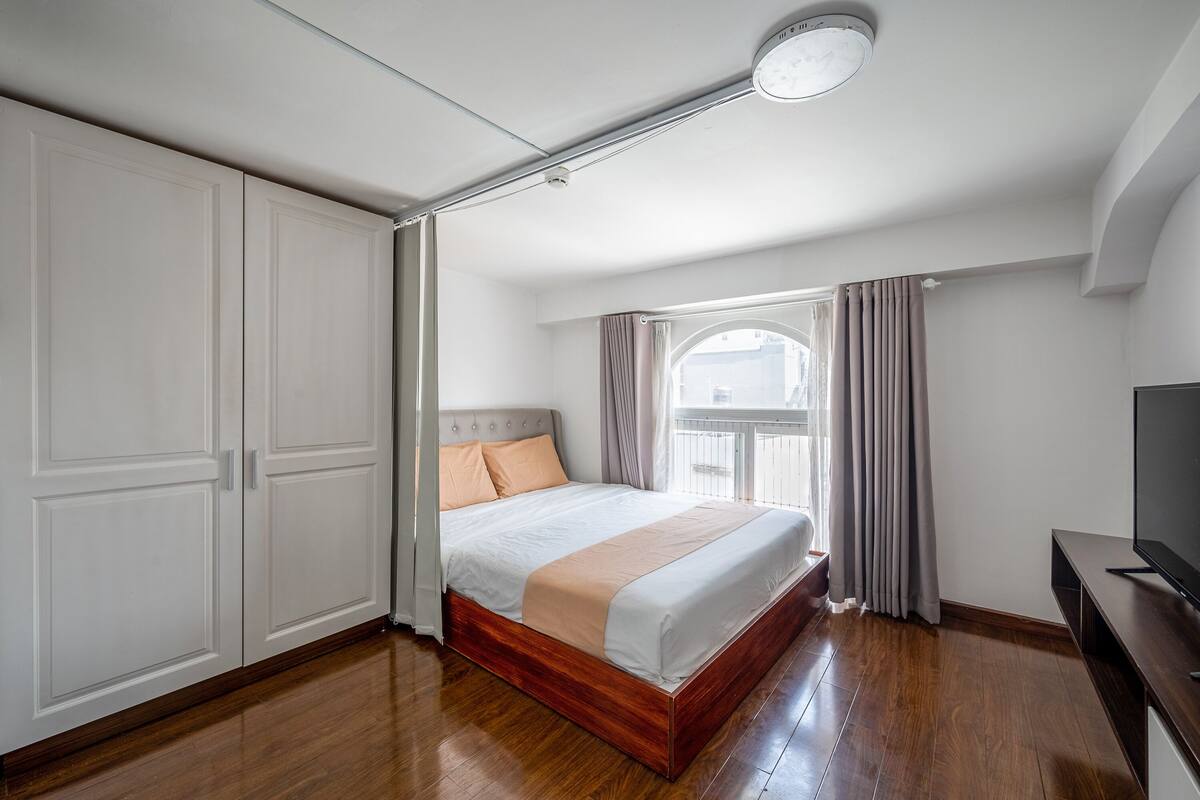 A bedroom with a bed, a wardrobe, a television, and a window with curtains.