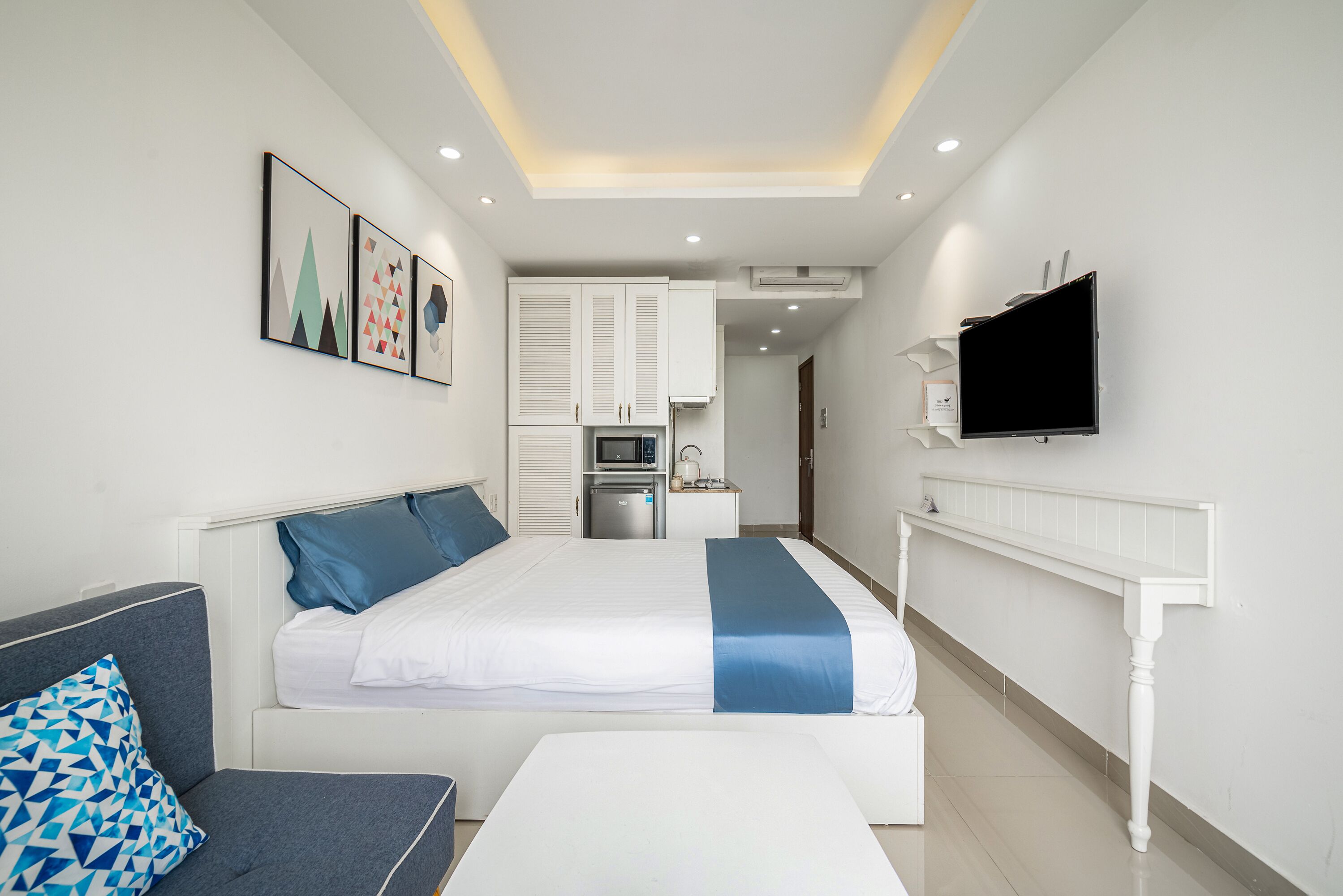 Una habitación de hotel moderna con cama, sofá, televisión y kitchenette.