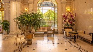Eine großzügige Lobby mit einem hohen Bogenfenster, einer Couch, Sesseln, einem Couchtisch und Topfpflanzen.